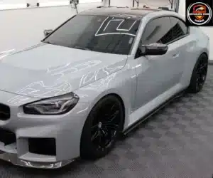 Front three-quarter view of a light gray sports car parked indoors on a checkered floor.